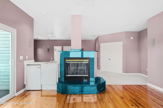 unfurnished living room featuring a fireplace, wood-type flooring, ceiling fan, and sink