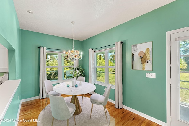 dining space featuring plenty of natural light, light hardwood / wood-style floors, a textured ceiling, and an inviting chandelier