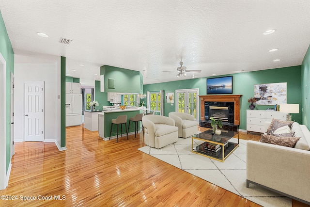 living room featuring a fireplace, a textured ceiling, light hardwood / wood-style floors, and ceiling fan