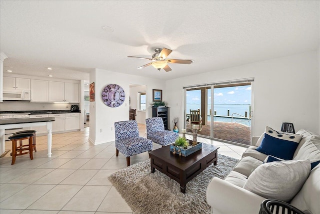 tiled living room featuring a water view, a textured ceiling, and ceiling fan