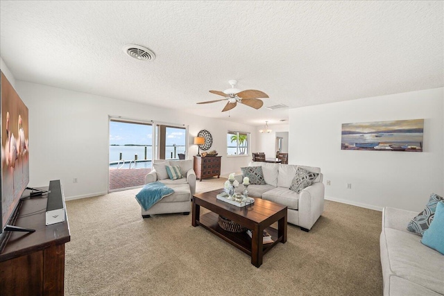 carpeted living room with ceiling fan, a water view, and a textured ceiling