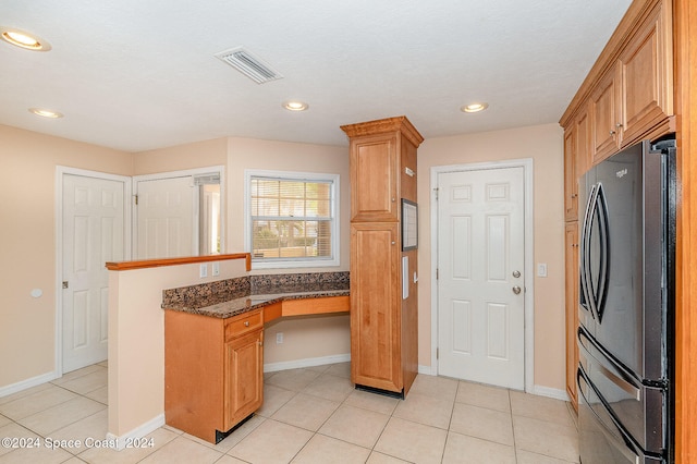 kitchen featuring fridge, light tile patterned floors, and dark stone countertops