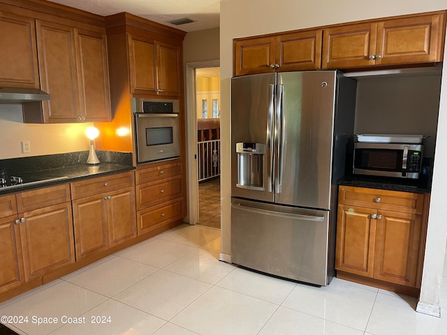 kitchen featuring dark stone countertops, light tile patterned floors, exhaust hood, and appliances with stainless steel finishes