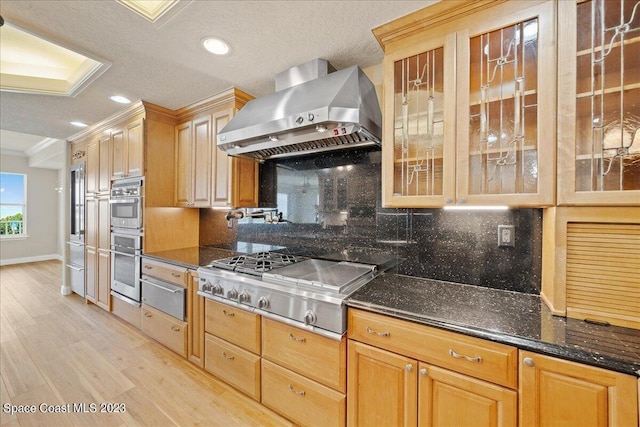 kitchen featuring wall chimney range hood, stainless steel appliances, dark stone counters, tasteful backsplash, and crown molding