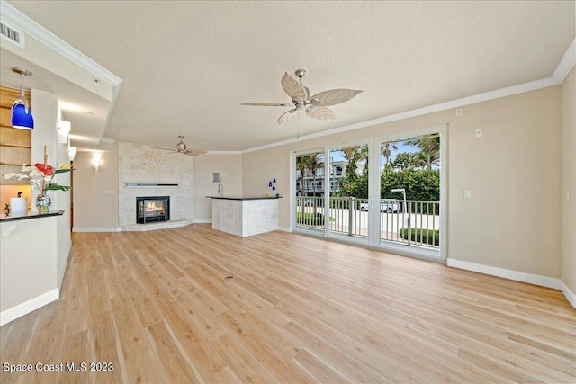 unfurnished living room featuring ceiling fan, light wood-type flooring, a fireplace, and ornamental molding