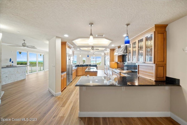 kitchen with stove, wall chimney exhaust hood, kitchen peninsula, and pendant lighting