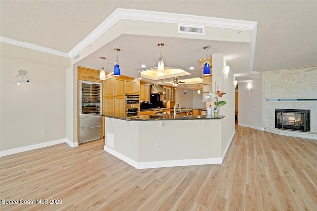 kitchen featuring decorative light fixtures, kitchen peninsula, a tray ceiling, a multi sided fireplace, and ornamental molding