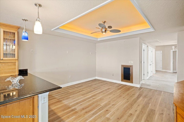 interior space featuring ceiling fan, light wood-type flooring, hanging light fixtures, and a tray ceiling