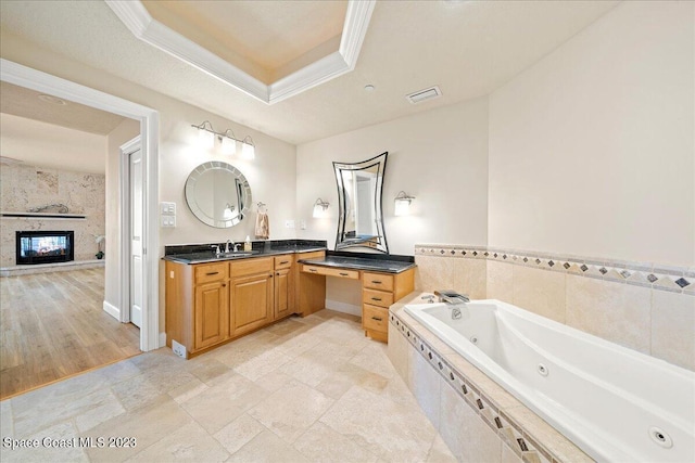 bathroom featuring vanity, wood-type flooring, a tray ceiling, ornamental molding, and a relaxing tiled tub