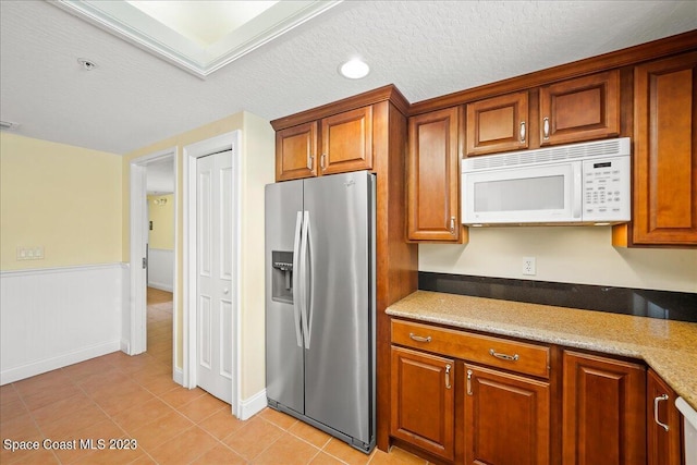 kitchen featuring light tile patterned floors, stainless steel refrigerator with ice dispenser, light stone counters, and a textured ceiling