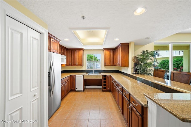 kitchen featuring white appliances, a textured ceiling, light tile patterned flooring, light stone counters, and a tray ceiling