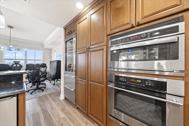 kitchen with decorative light fixtures, double oven, an inviting chandelier, light wood-type flooring, and crown molding