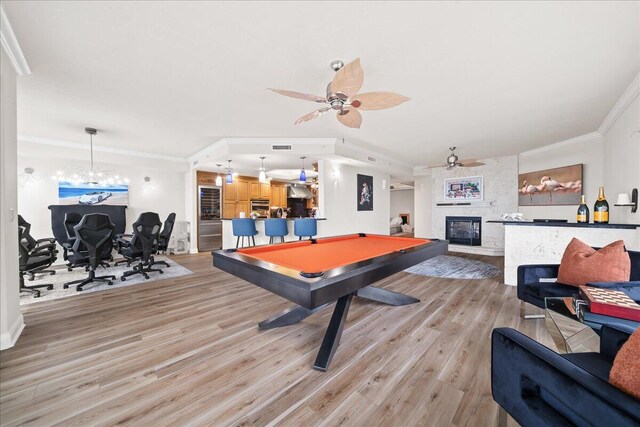 playroom featuring light hardwood / wood-style floors, a fireplace, billiards, ornamental molding, and ceiling fan with notable chandelier