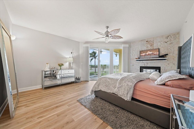 bedroom with ceiling fan, access to exterior, a large fireplace, and light hardwood / wood-style floors