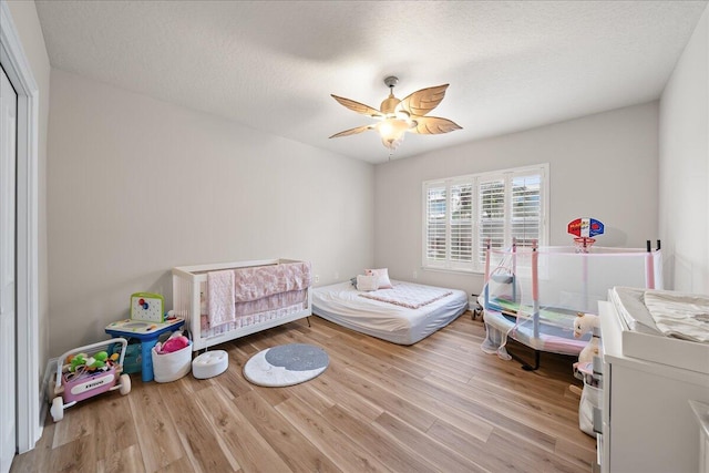 bedroom featuring a textured ceiling, ceiling fan, a nursery area, and light hardwood / wood-style flooring