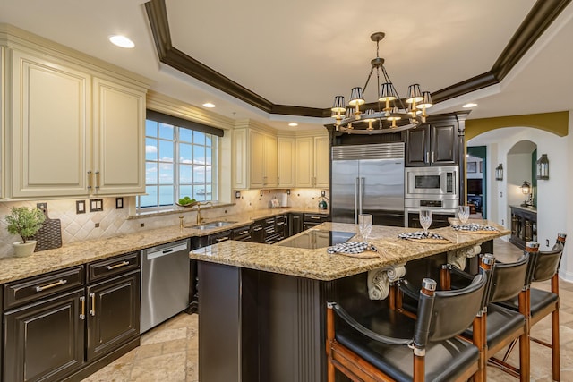 kitchen featuring a kitchen bar, built in appliances, a center island, a tray ceiling, and light stone countertops