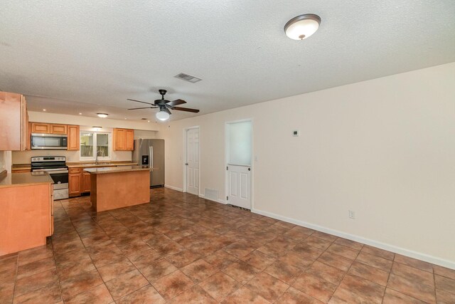 kitchen with a textured ceiling, a kitchen island, ceiling fan, tile patterned floors, and appliances with stainless steel finishes