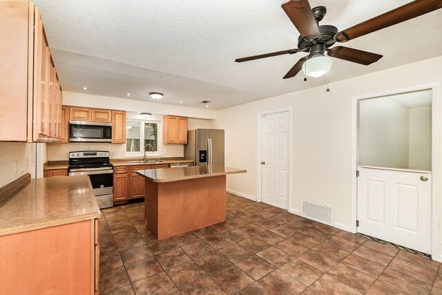 kitchen with a kitchen island, ceiling fan, stainless steel appliances, dark tile patterned flooring, and sink