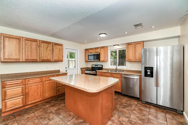 kitchen with dark tile patterned flooring, sink, appliances with stainless steel finishes, and a kitchen island