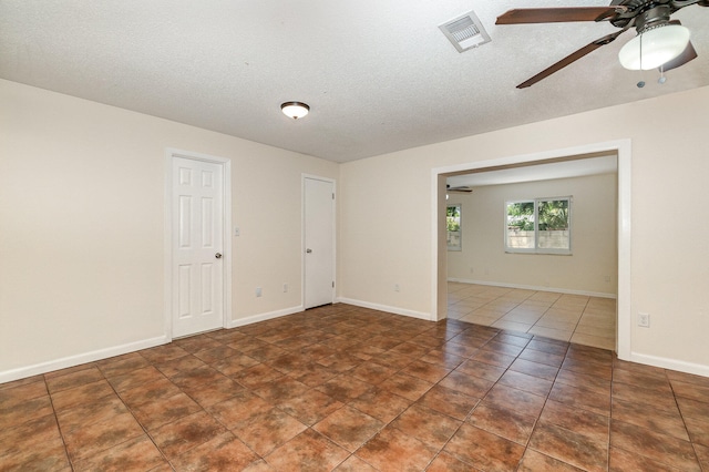 empty room with ceiling fan, a textured ceiling, and dark tile patterned floors