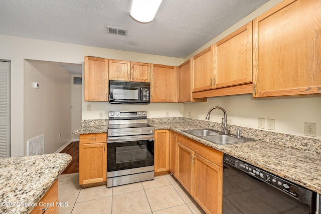 kitchen with light tile patterned floors, a textured ceiling, light stone countertops, black appliances, and sink