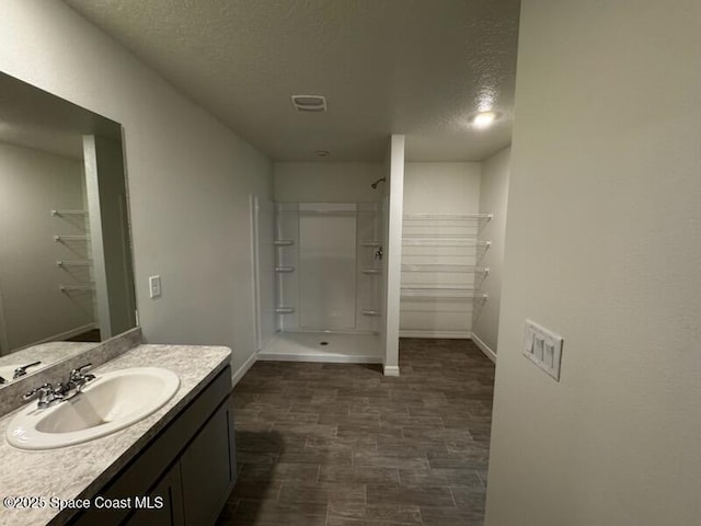 bathroom featuring walk in shower, vanity, and a textured ceiling