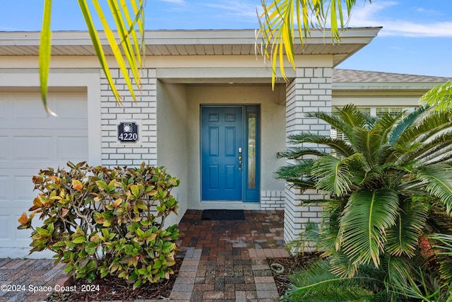 property entrance featuring brick siding, roof with shingles, and an attached garage