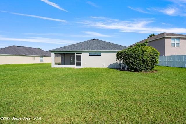 back of property with fence, a sunroom, roof with shingles, a lawn, and stucco siding