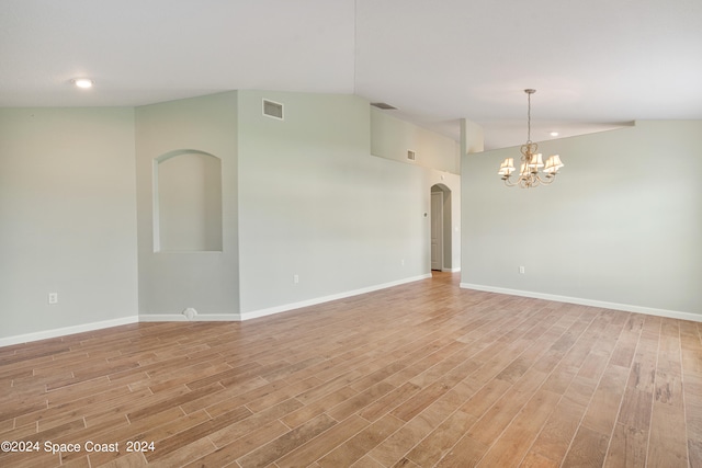 empty room featuring lofted ceiling, a notable chandelier, and light hardwood / wood-style floors