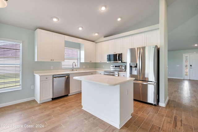 kitchen with vaulted ceiling, light wood-type flooring, appliances with stainless steel finishes, sink, and a kitchen island