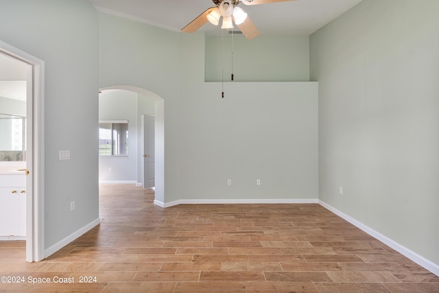 spare room featuring arched walkways, ceiling fan, a towering ceiling, baseboards, and light wood-type flooring