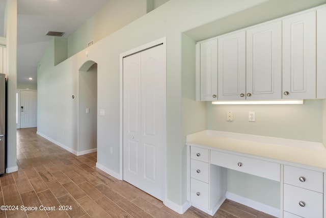 kitchen with light wood-type flooring, white cabinets, built in desk, and light countertops