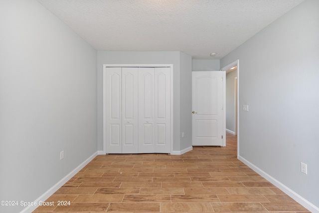 unfurnished bedroom featuring a textured ceiling, a closet, and light hardwood / wood-style floors