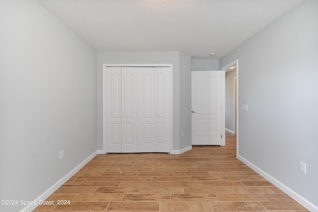 unfurnished bedroom with light wood-style floors, a textured ceiling, baseboards, and a closet