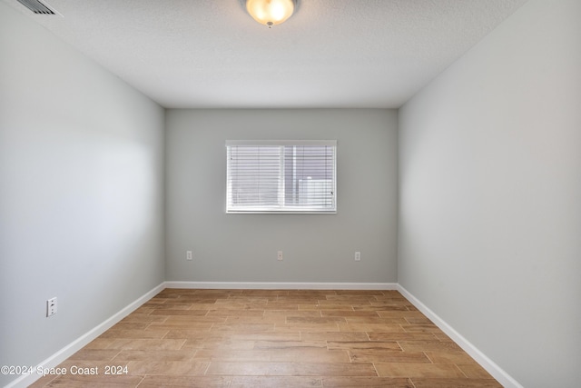 unfurnished room with light wood-style floors, visible vents, a textured ceiling, and baseboards