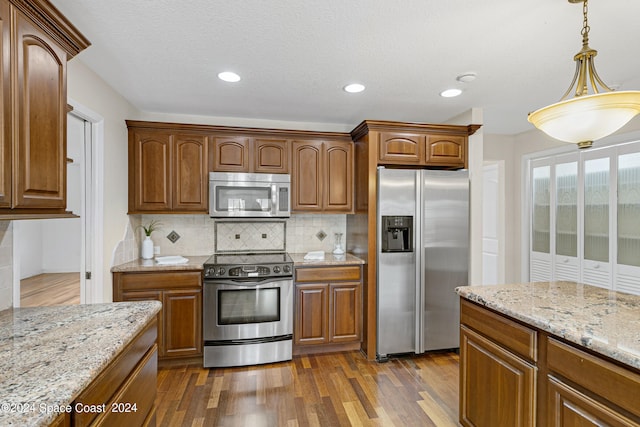 kitchen featuring light stone countertops, decorative light fixtures, dark hardwood / wood-style flooring, appliances with stainless steel finishes, and tasteful backsplash