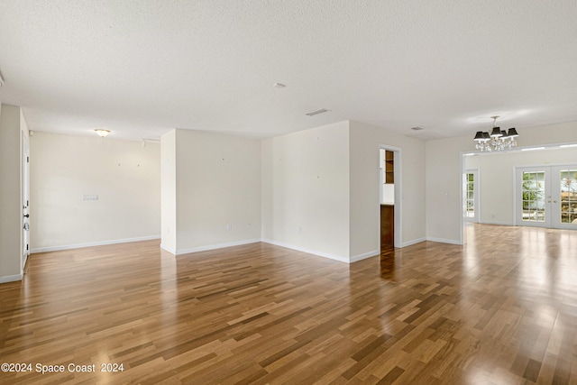 unfurnished living room with a textured ceiling, wood-type flooring, and a notable chandelier