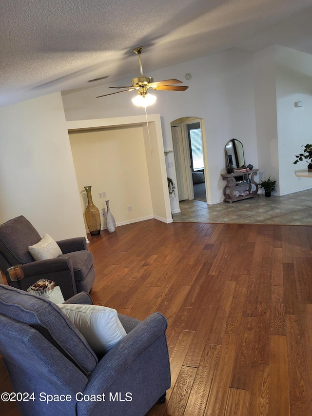 living room with dark wood-type flooring, ceiling fan, and a textured ceiling