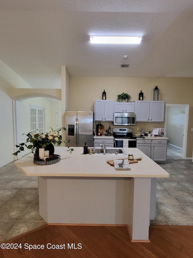 kitchen with appliances with stainless steel finishes, an island with sink, a textured ceiling, white cabinets, and light hardwood / wood-style flooring