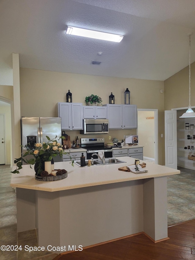 kitchen with white cabinets, hardwood / wood-style floors, hanging light fixtures, a kitchen island with sink, and stainless steel appliances