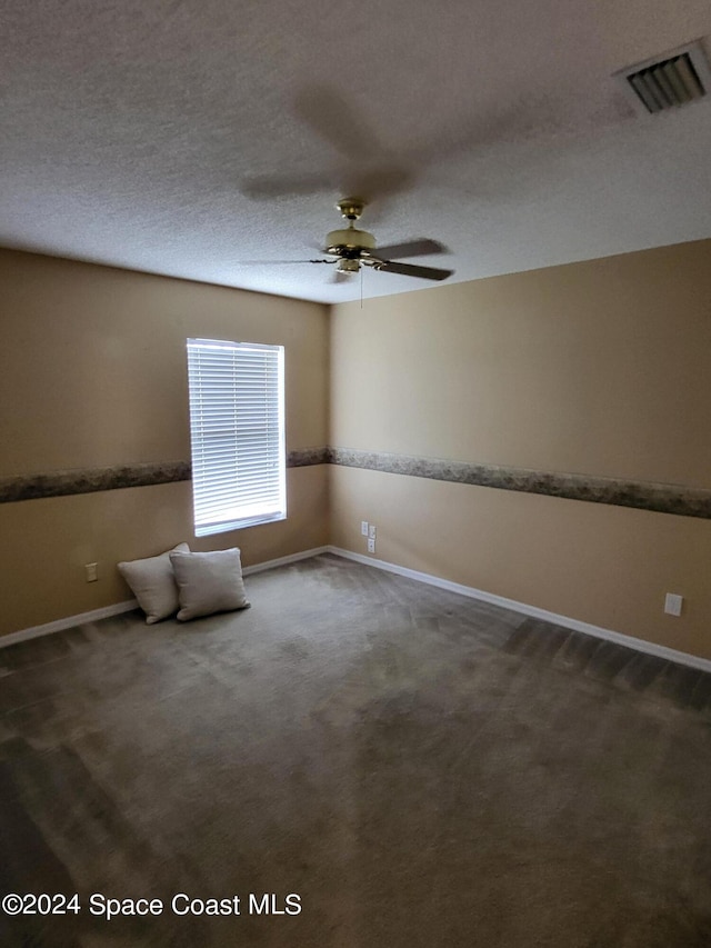 empty room with ceiling fan, a textured ceiling, and dark colored carpet