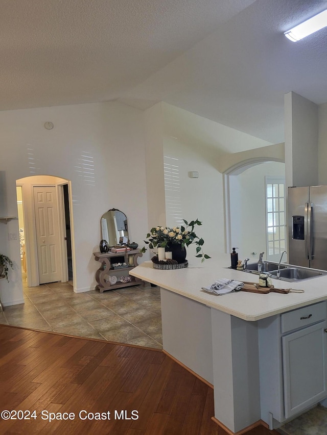 kitchen featuring lofted ceiling, stainless steel fridge, hardwood / wood-style floors, a textured ceiling, and sink