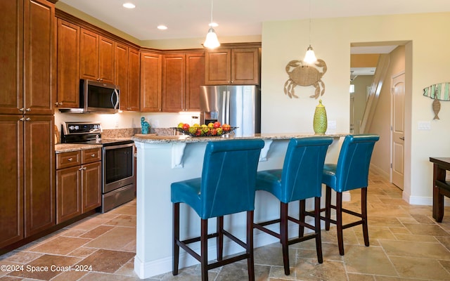 kitchen featuring a kitchen island, light stone countertops, decorative light fixtures, a breakfast bar, and stainless steel appliances