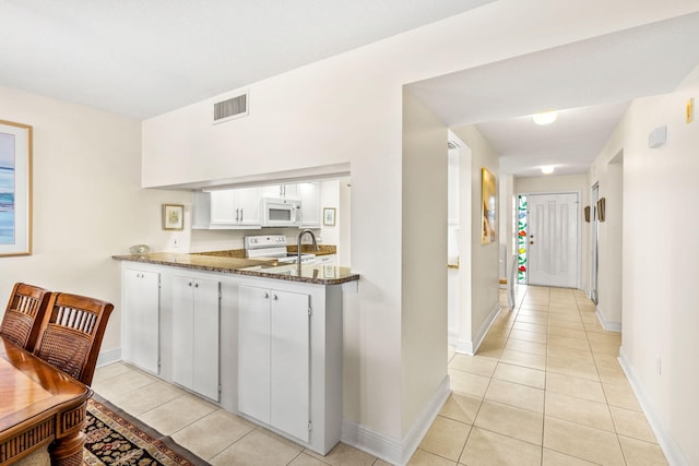 kitchen featuring light tile patterned flooring, dark stone countertops, white cabinets, and white appliances