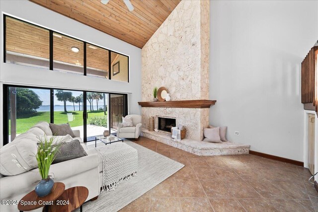 living room featuring high vaulted ceiling, ceiling fan, wood ceiling, and a stone fireplace