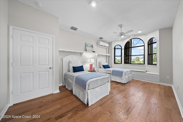 bedroom with ceiling fan, an AC wall unit, and hardwood / wood-style flooring