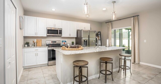 kitchen with appliances with stainless steel finishes, white cabinets, light tile patterned floors, and an island with sink