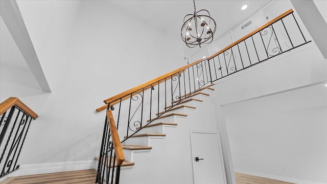 stairway with a notable chandelier, hardwood / wood-style floors, and a high ceiling