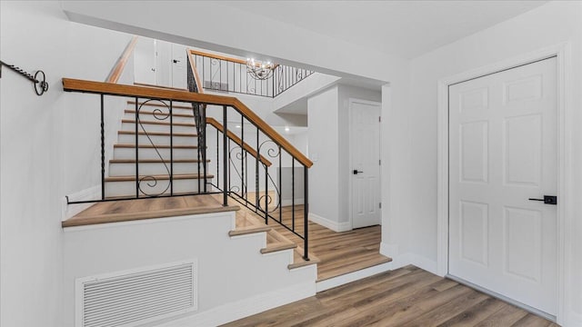 stairs with hardwood / wood-style flooring and a notable chandelier