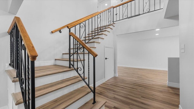 stairway with hardwood / wood-style flooring and a towering ceiling